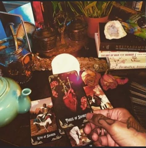 A candlelit tarot reading in progress, with the Three of Swords and King of Swords laid out among crystals and books